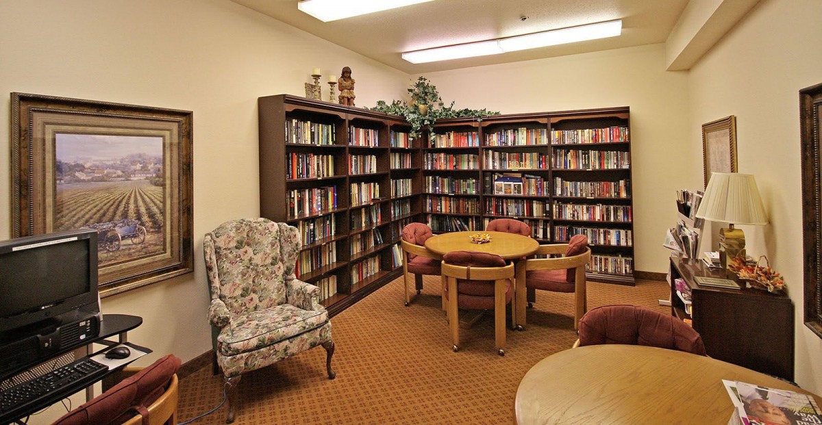 A cozy library corner with bookshelves, an armchair, and a small table surrounded by chairs.