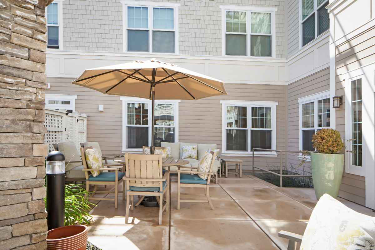 A cozy outdoor patio area featuring a table with chairs and an umbrella, set against the backdrop of a building exterior with multiple windows.