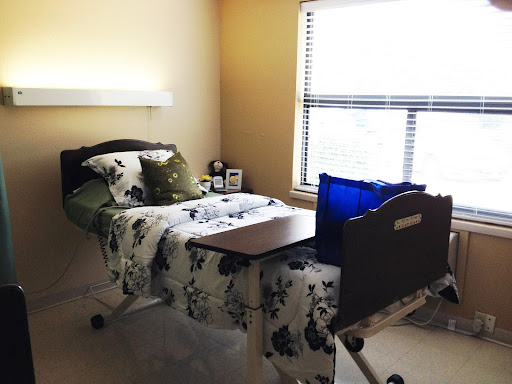 A cozy bedroom featuring a hospital bed, decorative bedding, and natural light from the window.