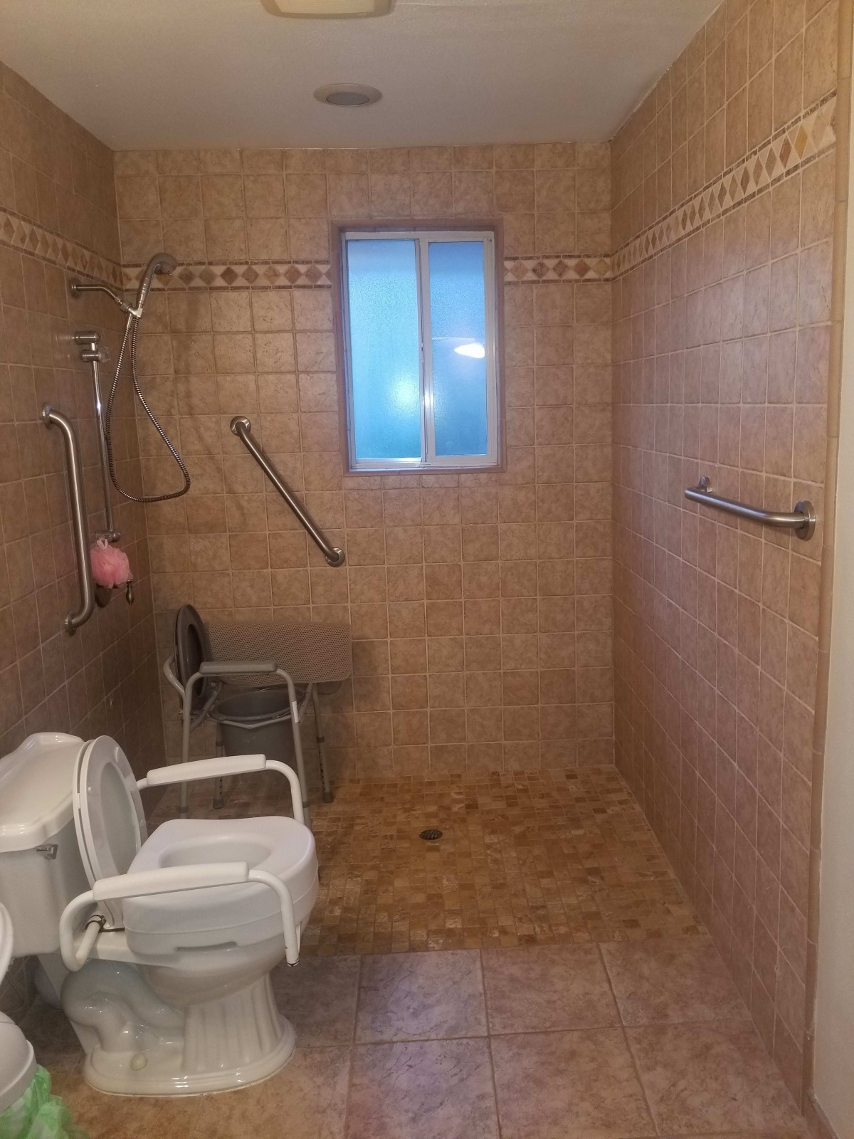 An accessible bathroom with a tiled shower area, featuring grab bars and a shower chair for safety.