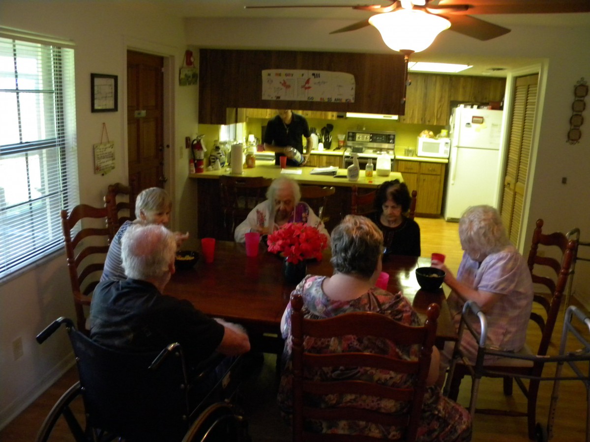 A group of seniors gathered around a dining table in a homey kitchen setting.