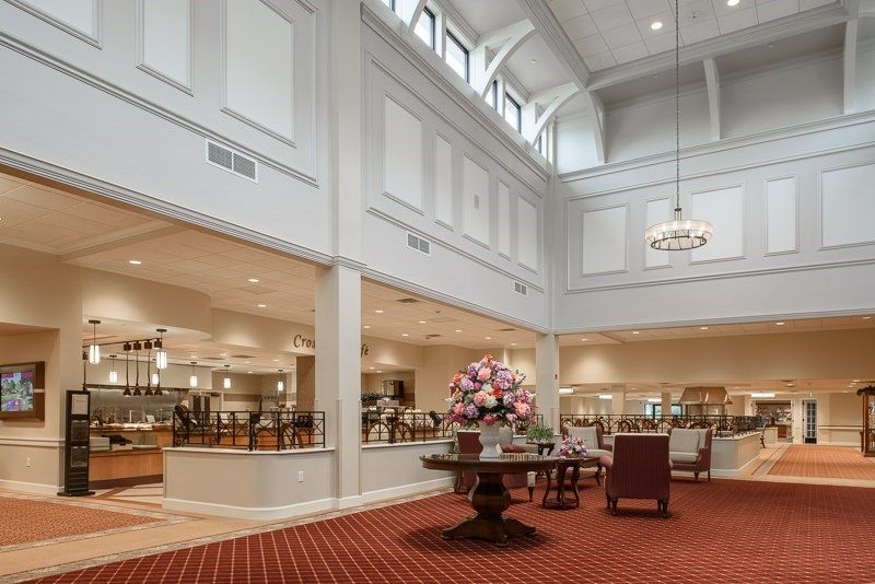 A spacious lobby with elegant architectural details, featuring a central floral arrangement and chandeliers.