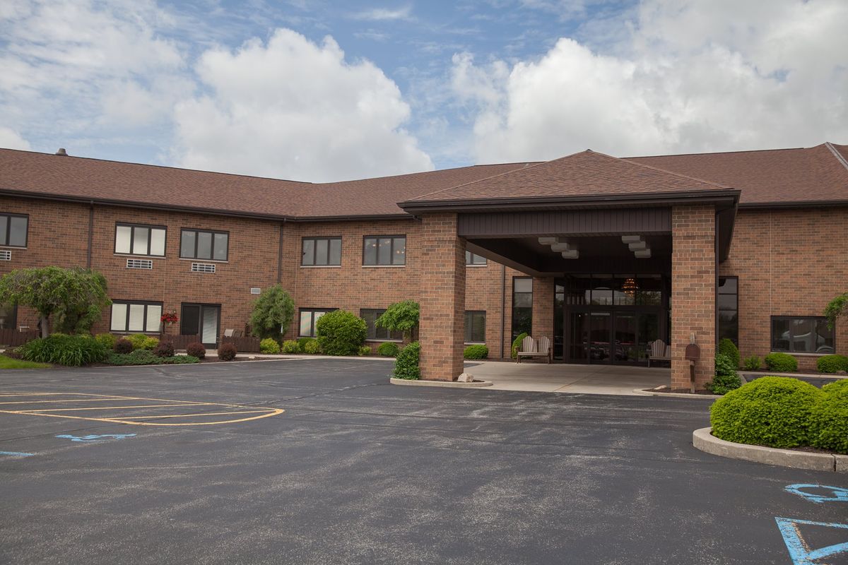 A two-story brick hotel with a covered entrance and a surrounding parking area under a cloudy sky.