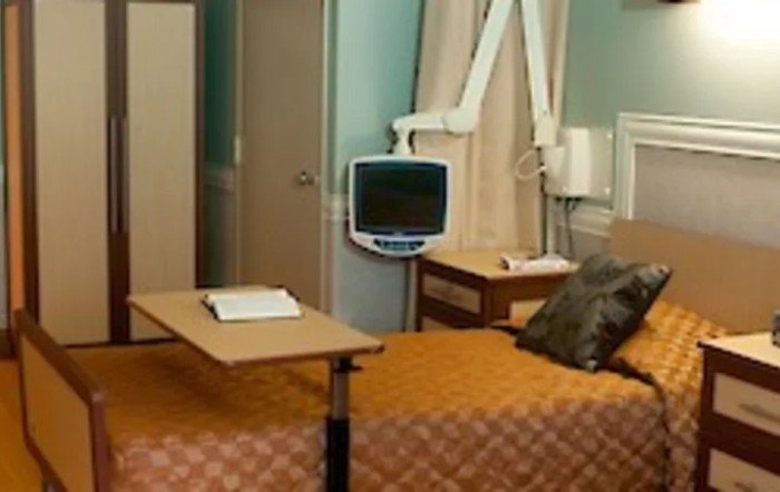 A hospital room featuring a bed, medical monitor, and bedside table.