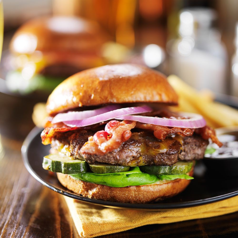A delicious cheeseburger topped with bacon, onions, and cucumbers served on a plate.