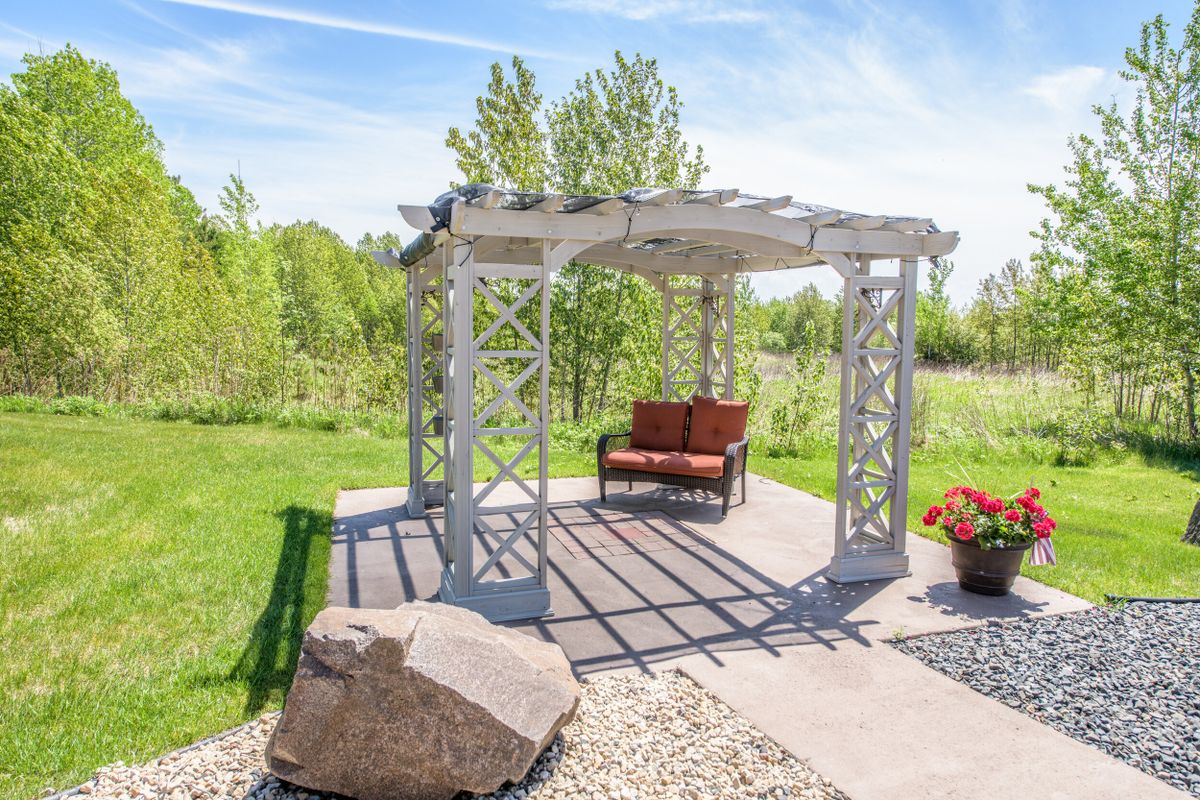 A sunny outdoor garden featuring a pergola with a bench underneath.