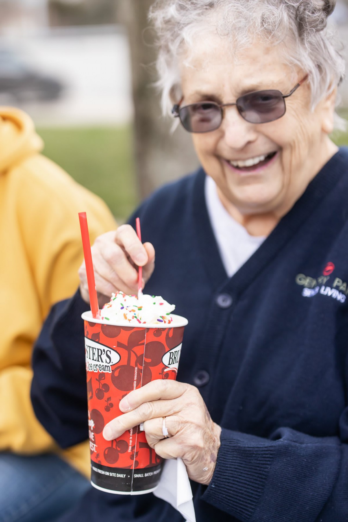 A smiling senior enjoys a cup of ice cream outdoors.