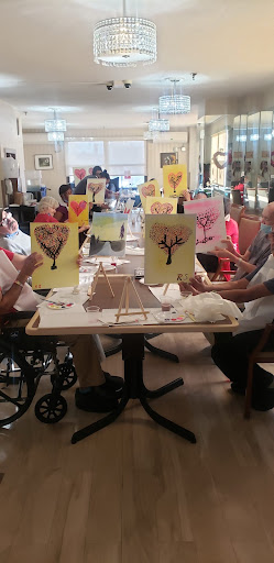 A group of elderly individuals enjoys a painting session, showcasing their artwork and engaging in creative expression.