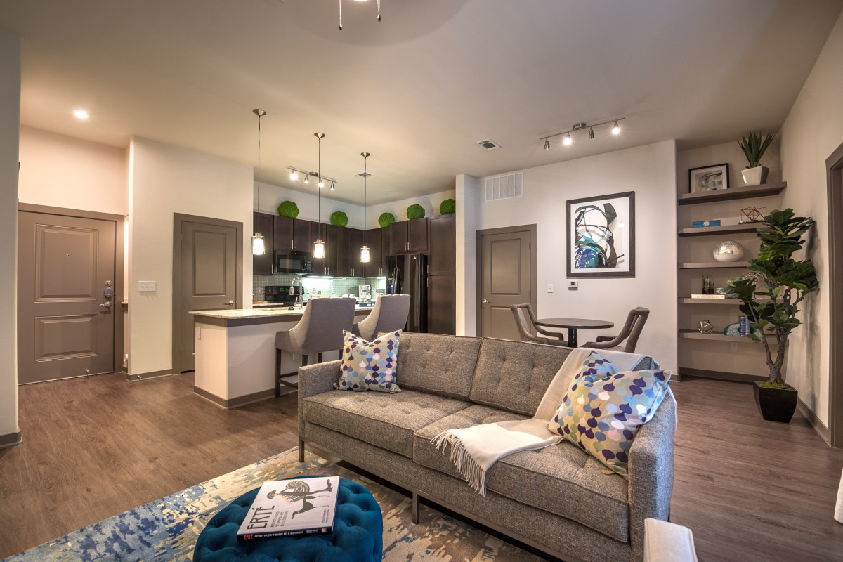 A modern, open-concept living space featuring a cozy sofa, stylish decor, and a kitchen with bar seating.
