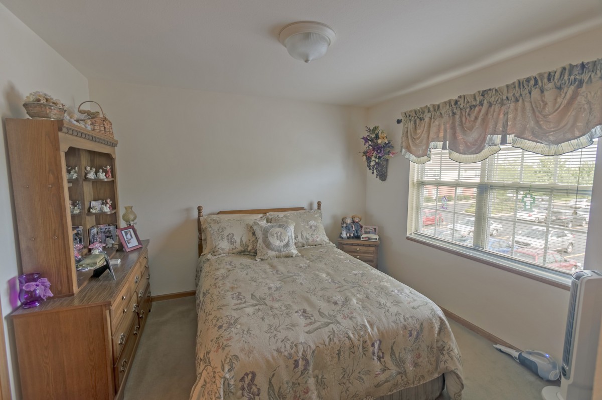 A cozy bedroom with a bed, dresser, and window with floral curtains.
