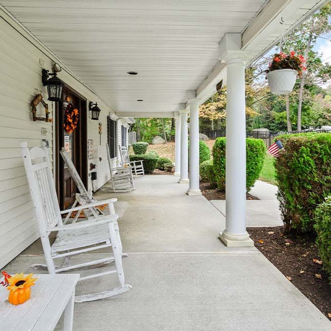 A cozy porch with white rocking chairs and decorative plants.