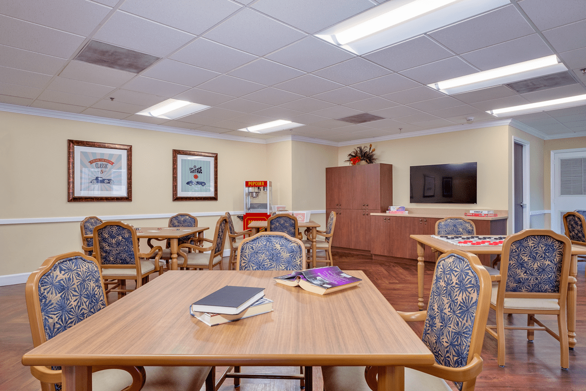 A community room with tables, chairs, a television, and books for activities.