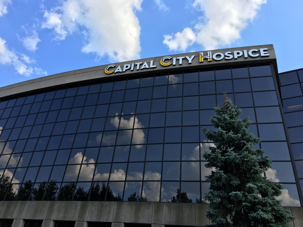 A modern building with a glass facade reflecting clouds, identified as Capital City Hospice.