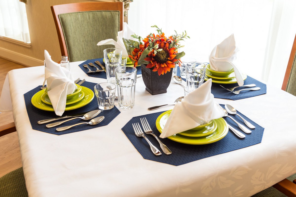 A beautifully arranged dining table with folded napkins, colorful plates, and a floral centerpiece.