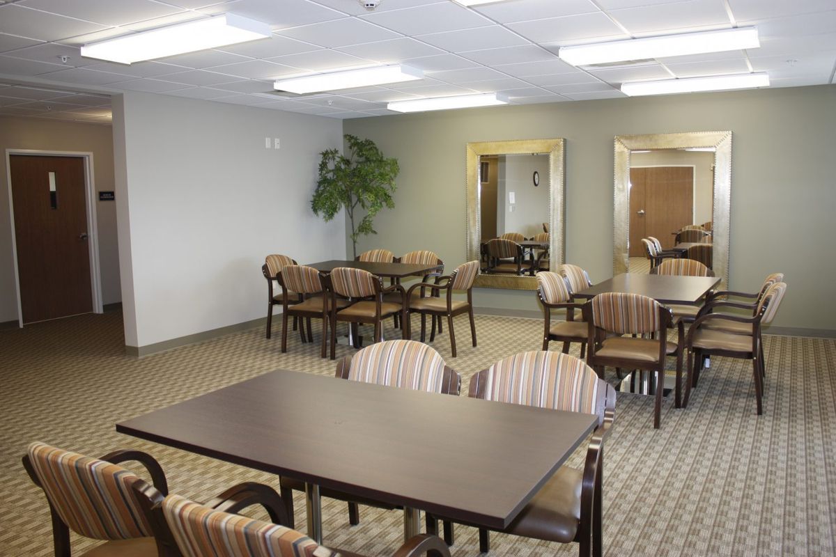 A simple dining area with multiple tables and chairs, featuring a large mirror and a potted plant for decoration.