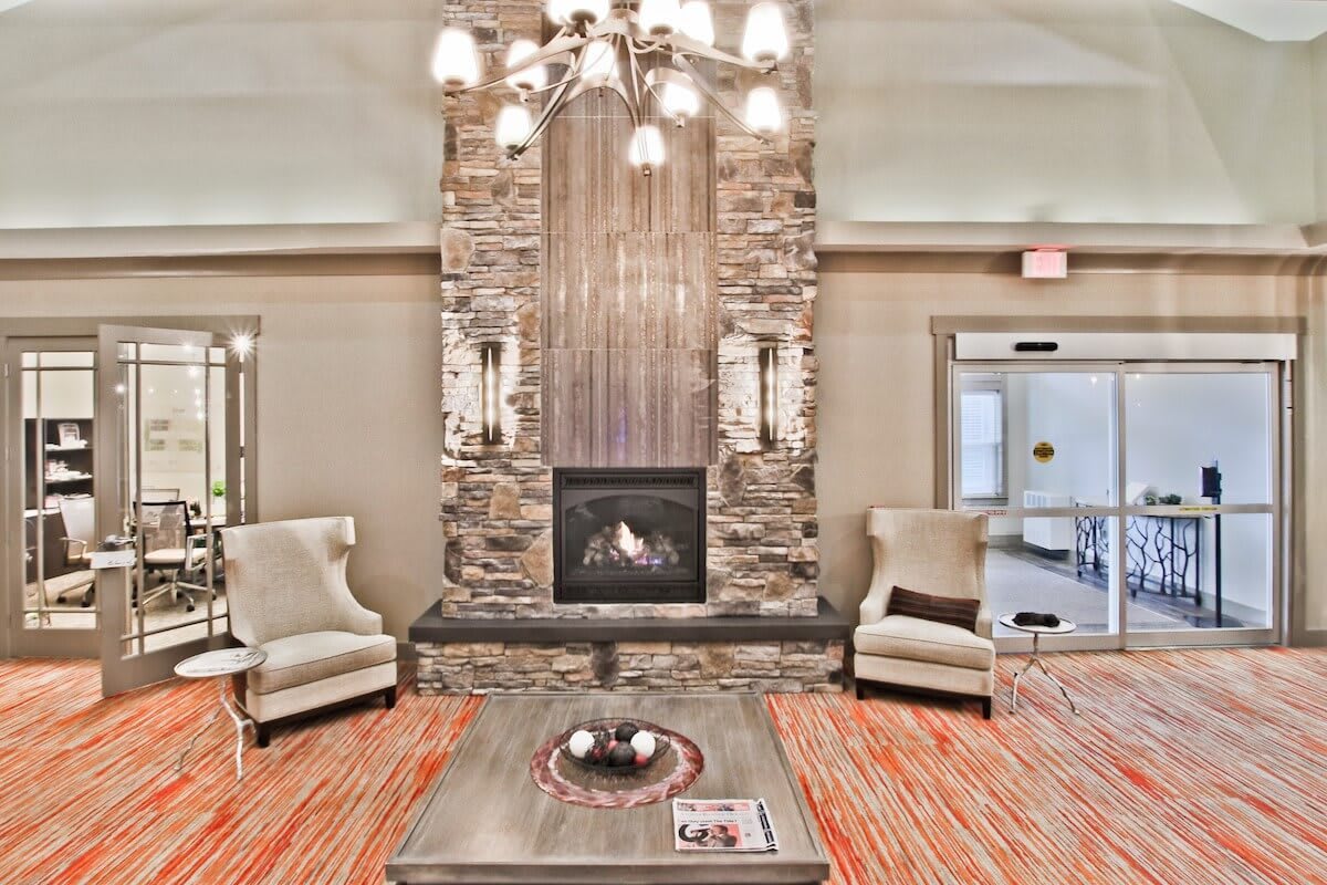 A cozy living room featuring a stone fireplace, armchairs, and a chandelier.