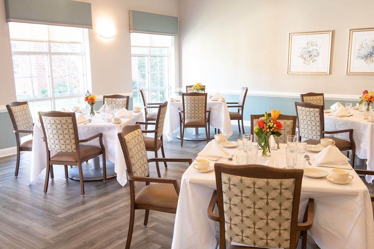 A bright and elegant dining area with tables set for guests, decorated with flowers and white tablecloths.