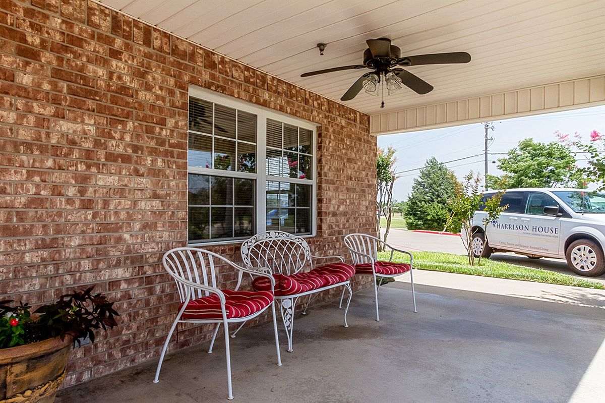 A cozy porch with brick walls featuring white metal chairs with red cushions and an overhead ceiling fan.