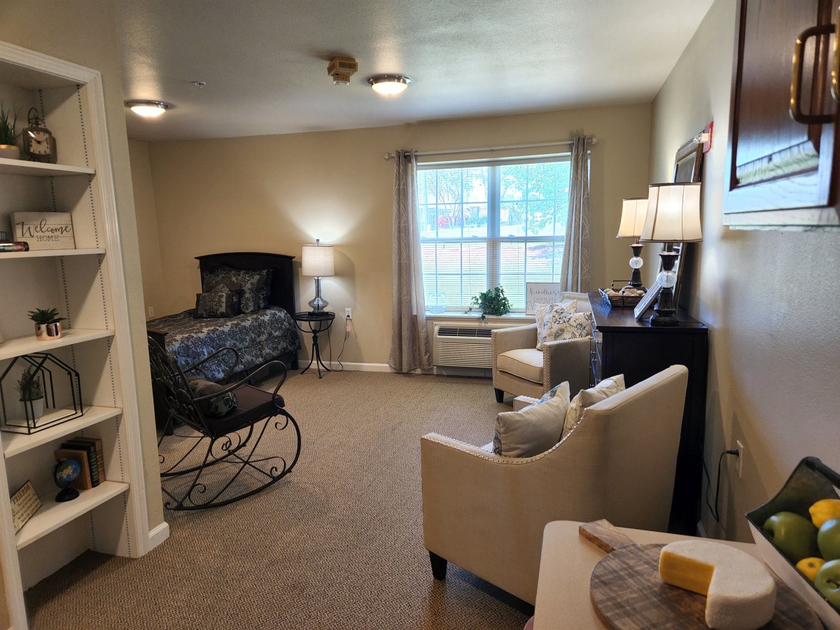 A cozy bedroom with a rocking chair, armchair, and bed next to a large window.