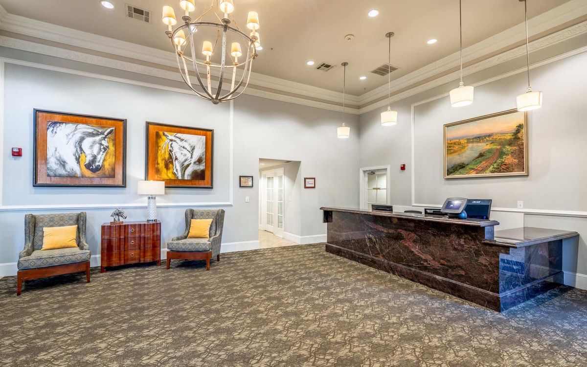 A spacious and elegantly decorated lobby with a reception desk, chandelier, and paintings on the walls.