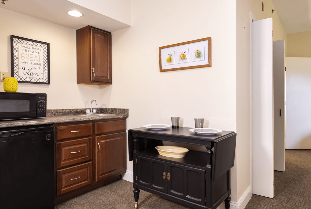 A compact kitchen space featuring wooden cabinets, a sink, and a small black cart with dishware.