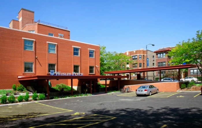 A brick hospital building with a parking lot and car on a clear day.