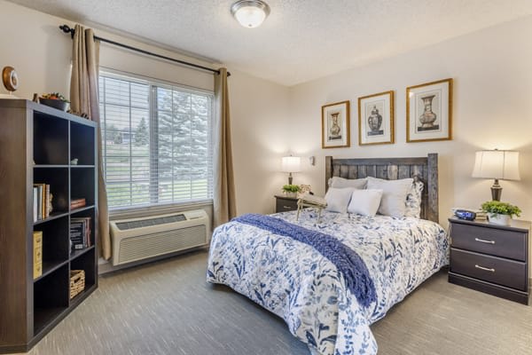 A cozy bedroom with a stylish bedspread, elegant artwork, and natural light coming through the window.