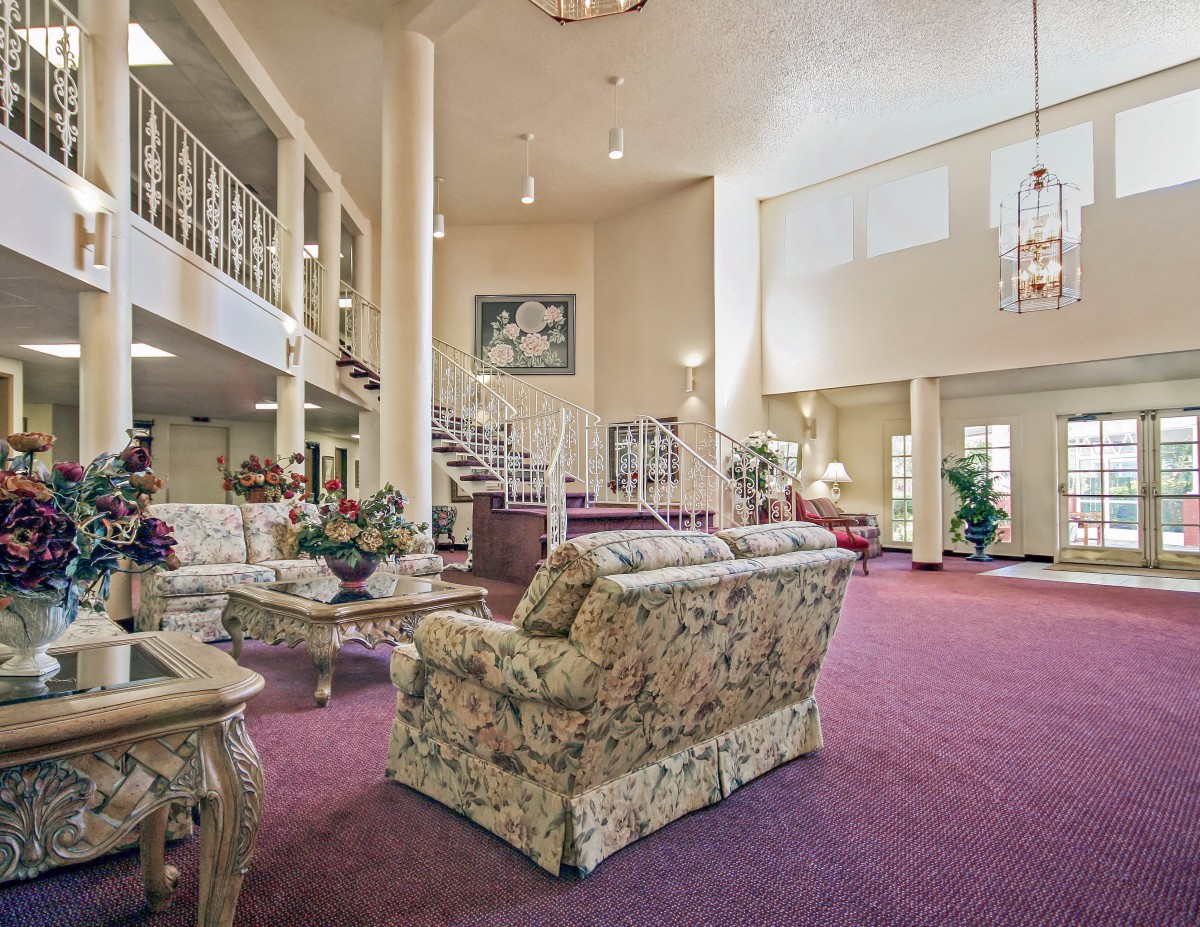 A spacious living room interior with elegant furniture, a grand staircase, and a chandelier.