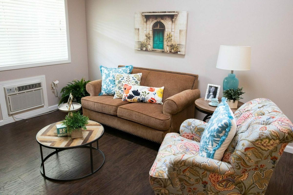 A cozy living room with a brown sofa, floral cushions, and a decorative armchair beside a round coffee table.