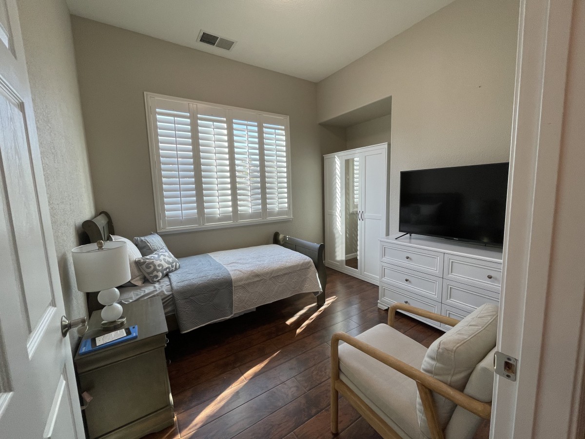 A well-lit bedroom with a bed, dresser, and TV.