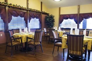 A cozy dining room with elegantly set tables and striped chairs, featuring decorative curtains.