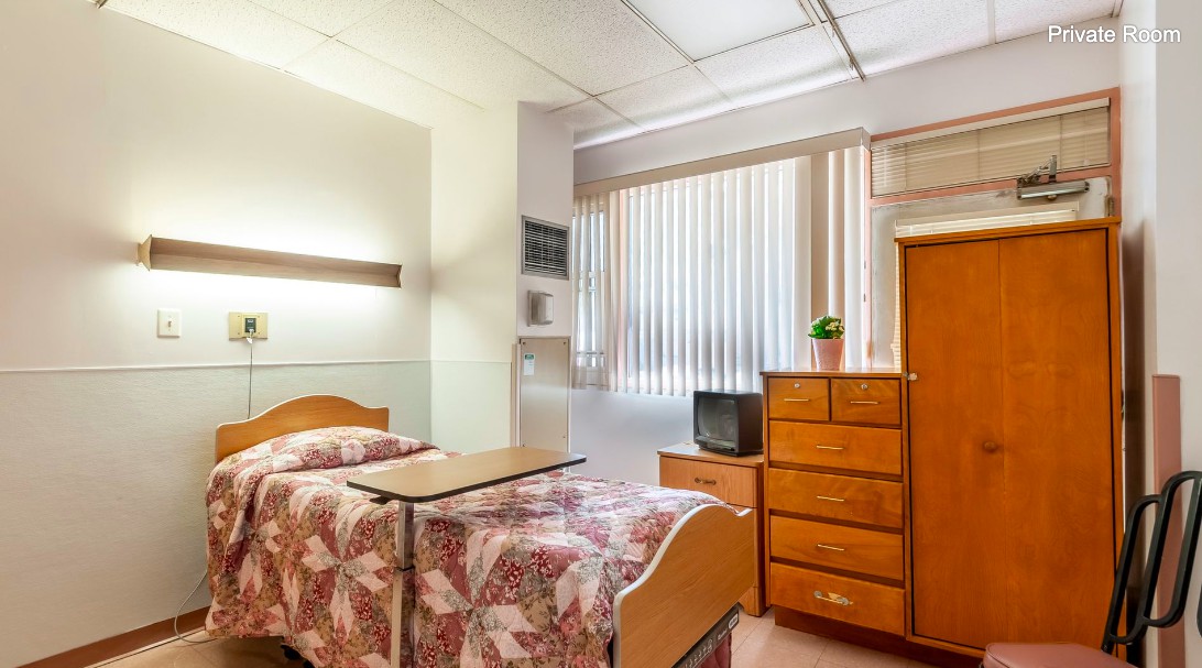 A hospital room with a single bed, wooden furniture, and a television.