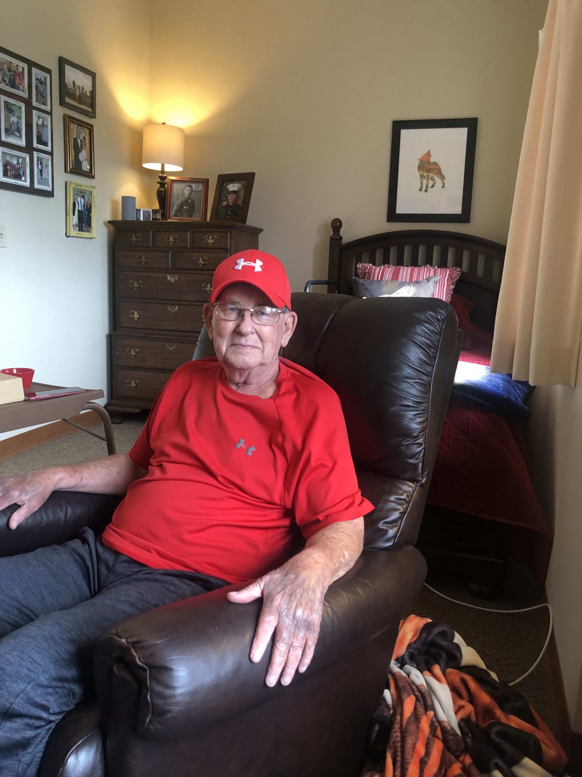 A man in a red shirt and cap sits comfortably in a chair in a living room.