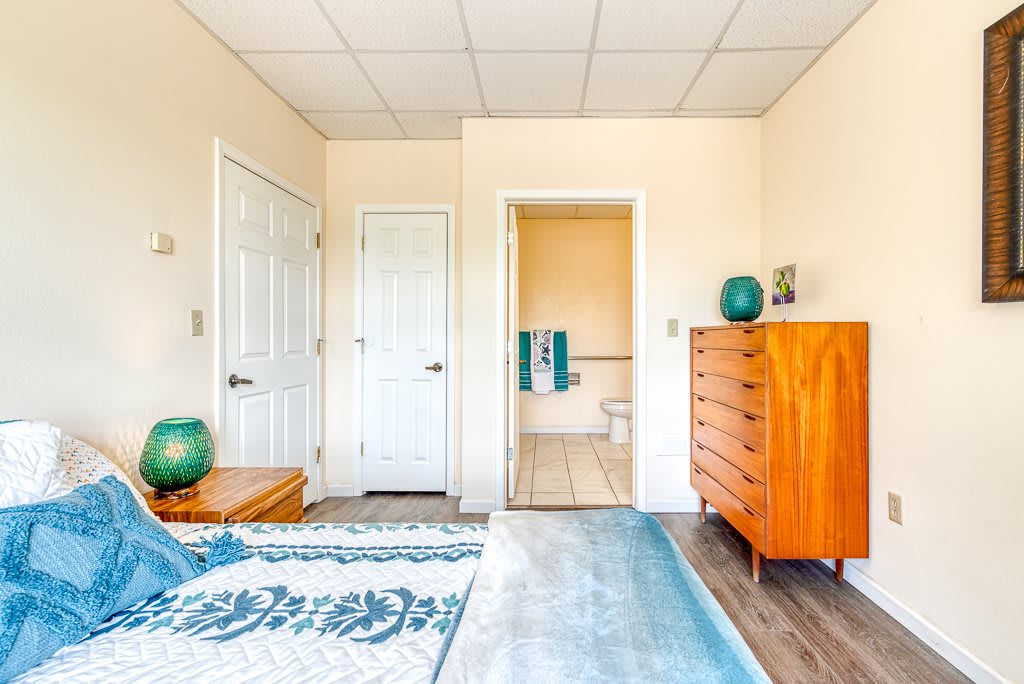 A cozy bedroom with a wooden dresser, bed, and an adjacent bathroom.