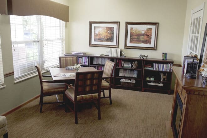 A cozy living room with a table and chairs, decorated with bookshelves and artwork on the walls.