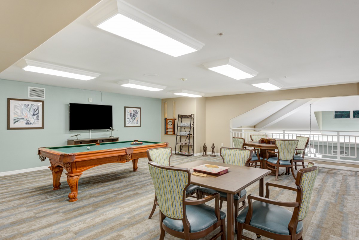 A well-lit recreation room featuring a pool table, multiple seating areas, and a television.