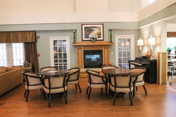 A cozy living room with tables and chairs arranged around a fireplace, complemented by a piano for an elegant touch.