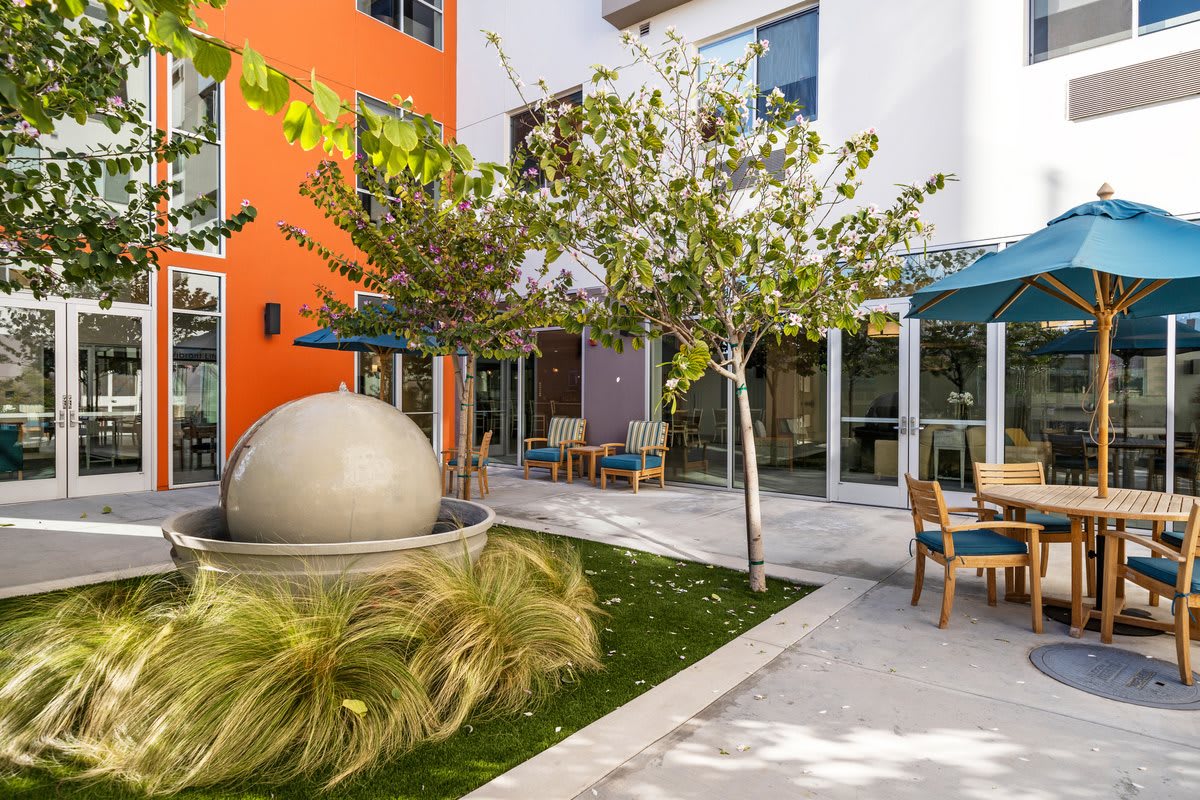 A modern courtyard with outdoor seating and a spherical art installation surrounded by greenery.