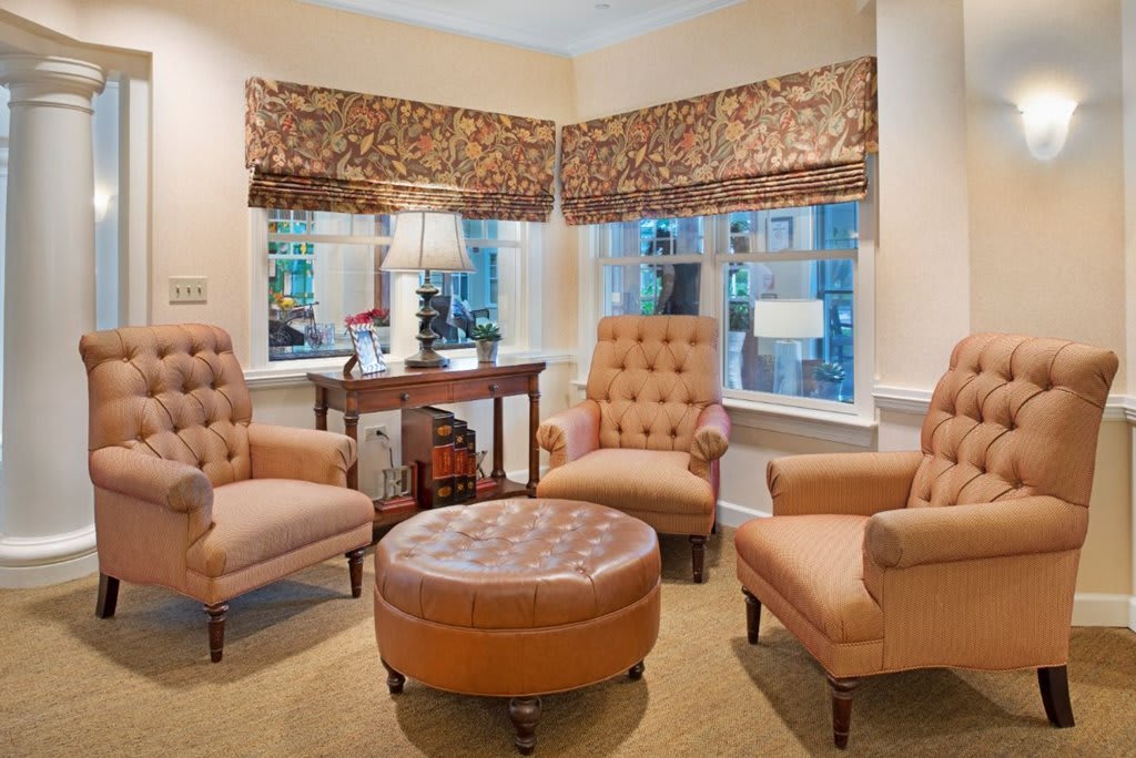 A cozy living room with comfortable chairs and a round ottoman, accented by patterned window treatments and soft lighting.
