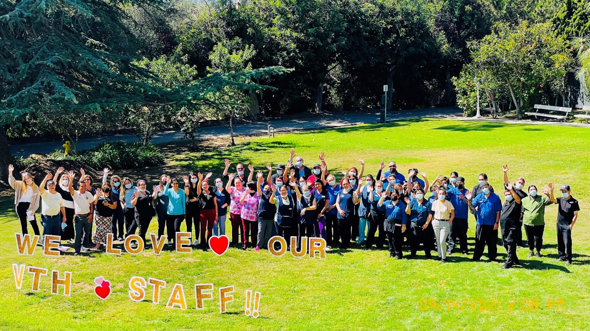 A group of staff members gathered outdoors, celebrating their teamwork and appreciation in a park setting.