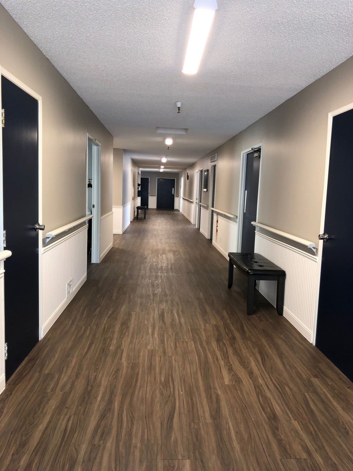 A long, well-lit corridor with multiple doors and a small seating area.