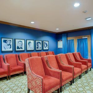 A small theater room with red upholstered chairs and framed photographs on the wall.