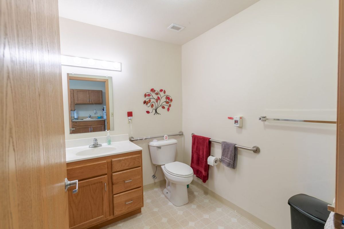 A clean and well-lit bathroom with a wooden cabinet, toilet, sink, mirror, and decorative wall art.