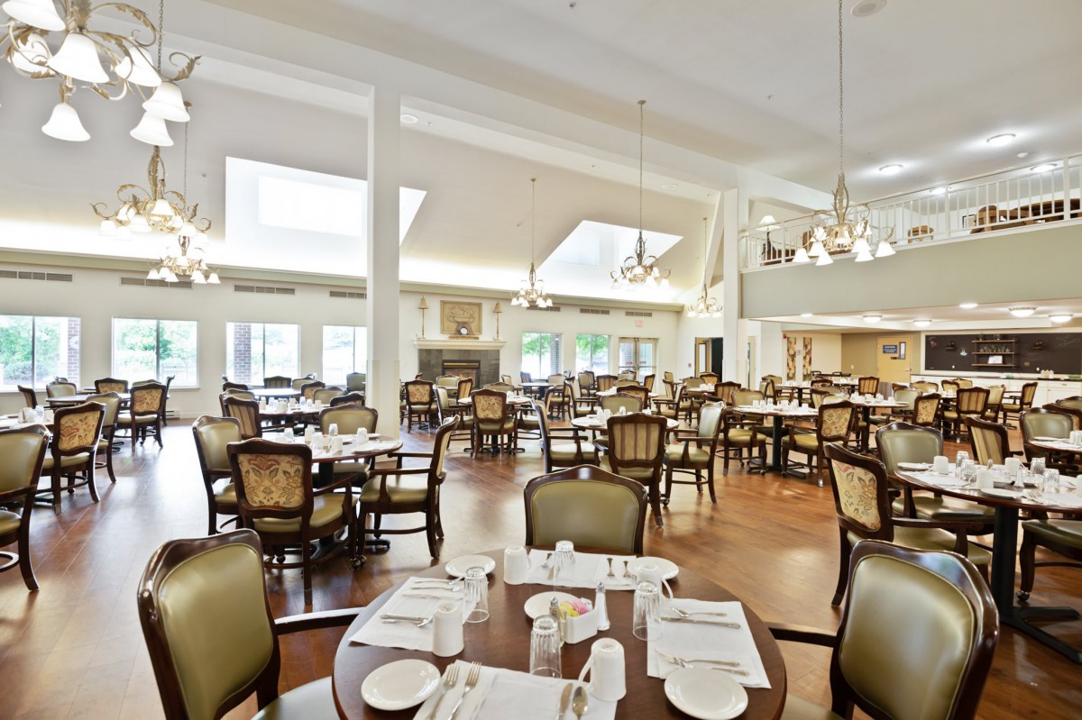 A spacious dining room with elegantly arranged tables and chairs, illuminated by natural daylight and chandeliers.