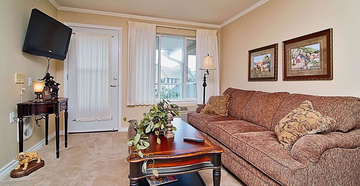 A cozy living room with a sofa, coffee table, and lamp in front of a window with curtains.