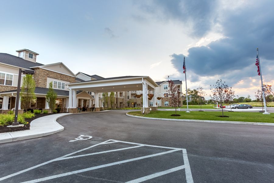 A large building with an entrance driveway and a flagpole in the parking lot under a cloudy sky.