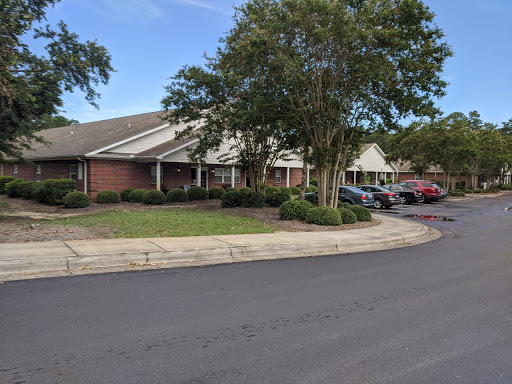 A quaint residential building surrounded by greenery and parked cars.