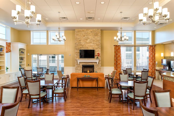 A spacious dining room interior with multiple tables and chairs, featuring a fireplace and elegant chandeliers.