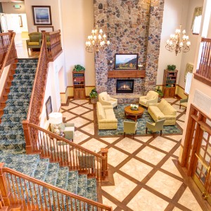 A spacious and elegantly designed living room with a grand staircase, chandeliers, and a fireplace.