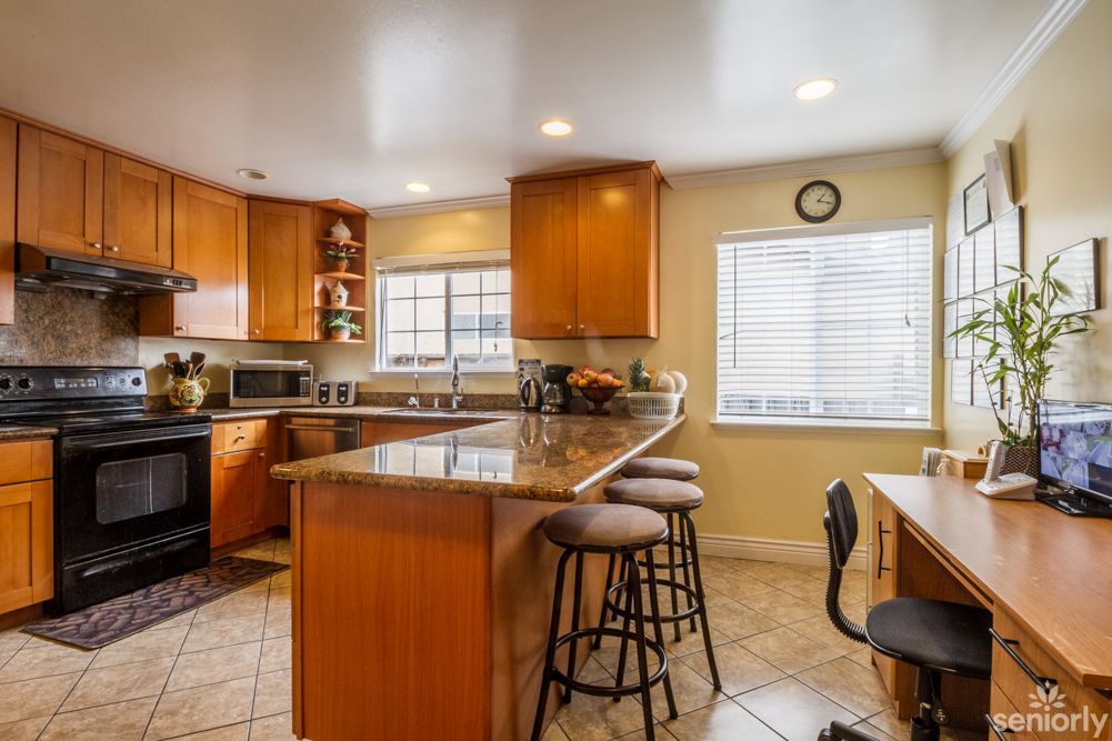 A modern kitchen with wooden cabinets, a granite countertop, bar stools, and various appliances.